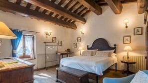 Ein Schlafzimmer mit Holzbalkendecke, einem Bett mit weißer Bettwäsche, einem Schreibtisch mit Lampe und einer Kommode.