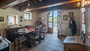 A cozy dining area with a wooden table and chairs, a window with curtains, and a view of the outdoors. - Casatorre 6 2 Emma Villas (Saludecio)