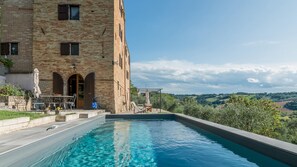 Ein Poolbereich mit Blick auf ein Backsteingebäude, Gartenmöbel und einer Pergola.