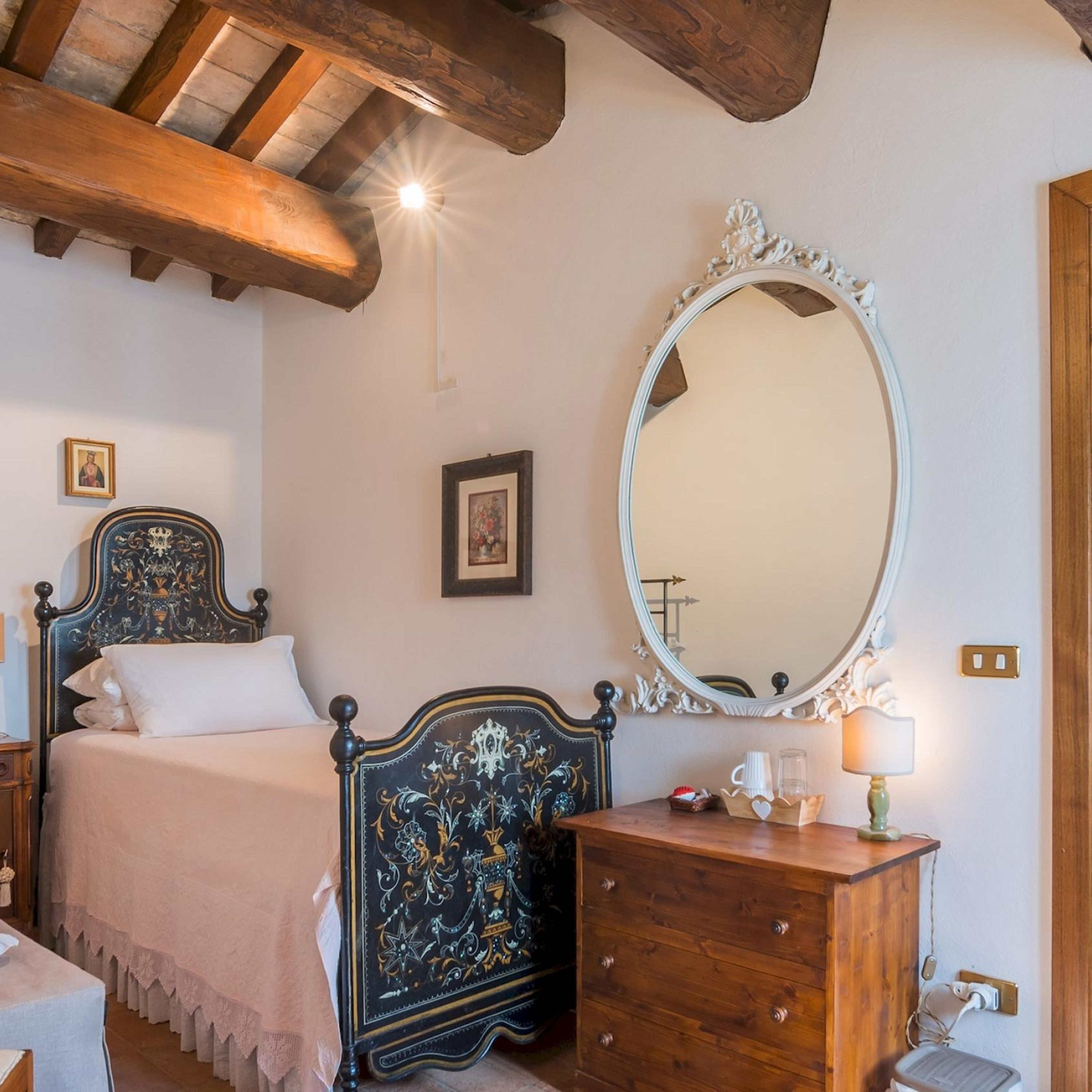 Een slaapkamer met een bed, een dressoir, een spiegel en een plafondlamp.