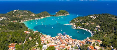 An aerial view of a coastal town with a marina, surrounded by hills and clear blue waters.