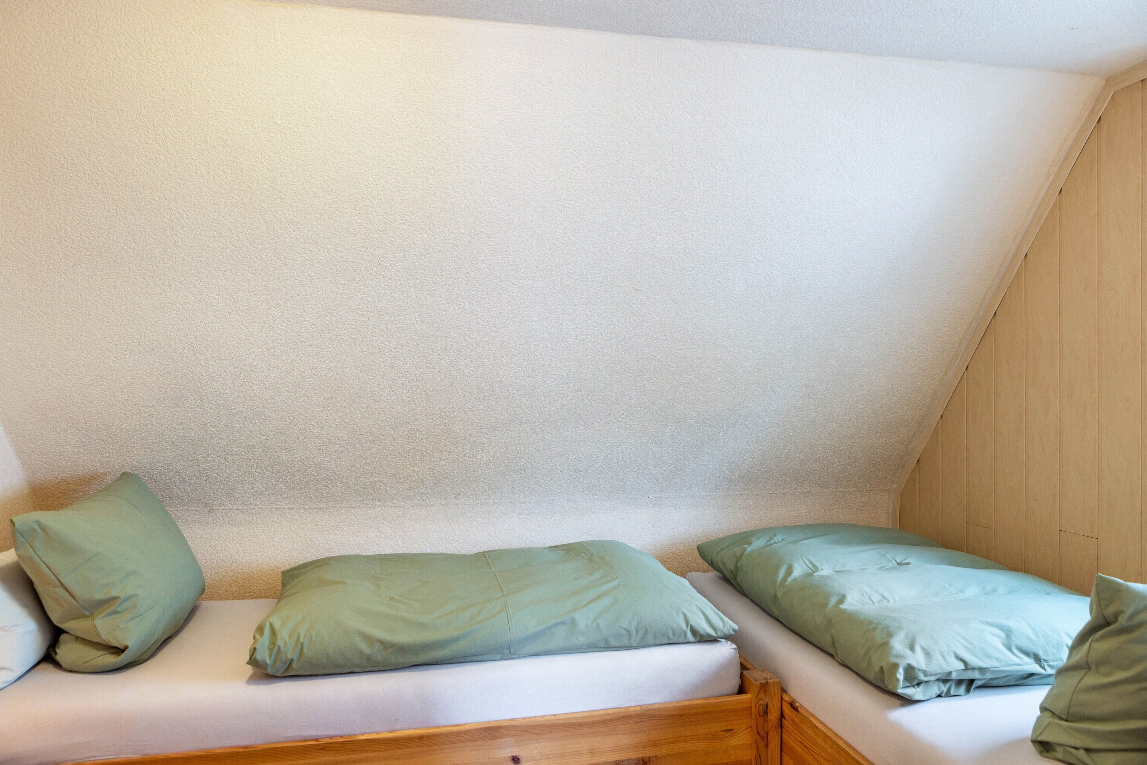 A small, cozy room with a single bed, a wooden headboard, and a sloped ceiling.