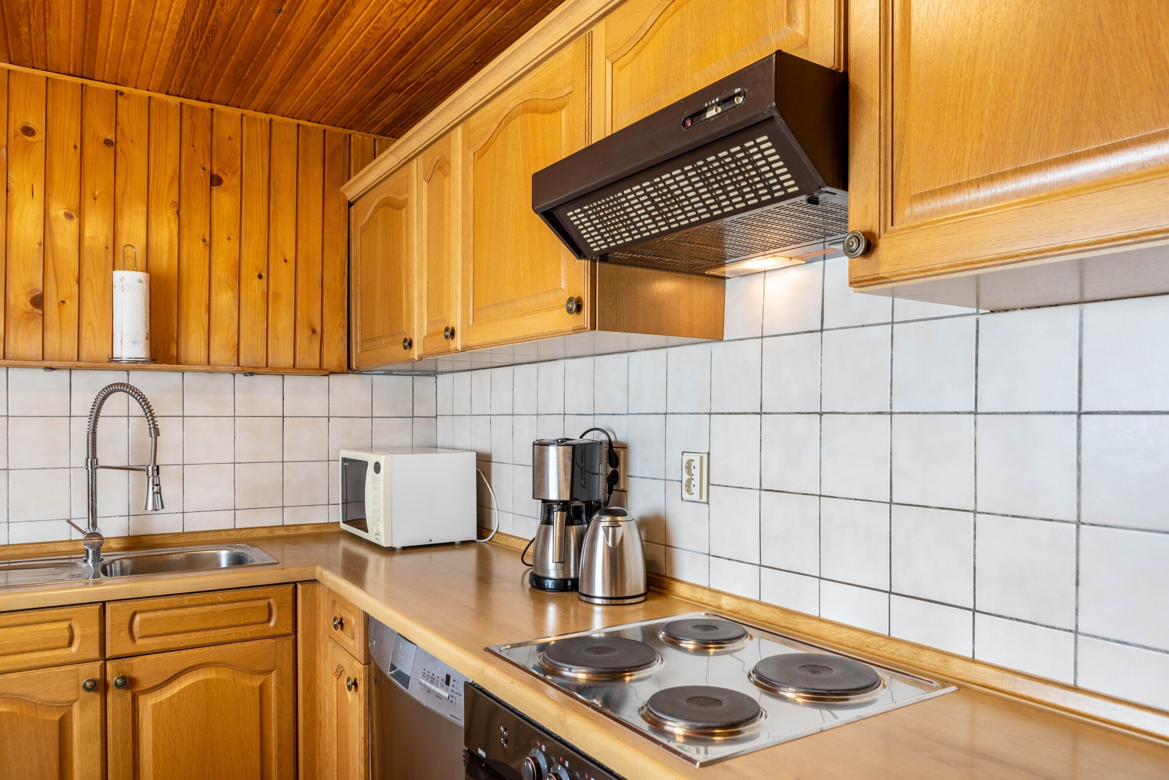 A kitchen with wooden cabinets, a stainless steel sink, a microwave, a coffee maker, and a stove.