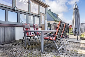 En uteplats med ett bord och stolar, en lyktstolpe och utsikt över ett hus med ett grönt tak.
