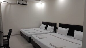 Une chambre d’hôtel avec trois lits simples, un bureau et un appareil de climatisation.