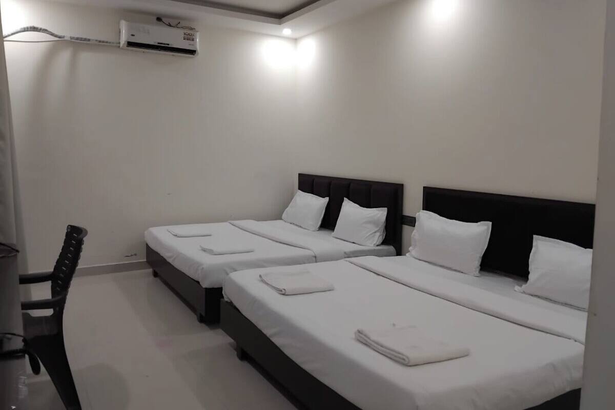 Ein Hotelzimmer mit drei Einzelbetten, einem Schreibtisch und einer Klimaanlage.
