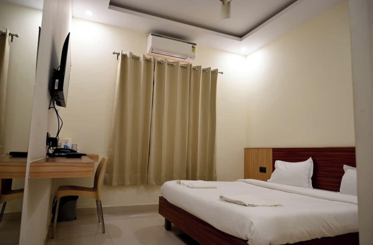 A hotel room with a bed, a desk, a chair, and a television.
