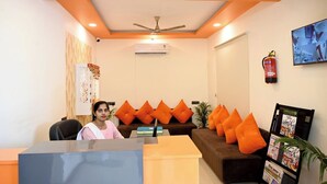 Un espace d’accueil comprenant un bureau, un canapé avec des coussins orange, un ventilateur de plafond et un extincteur fixé au mur.