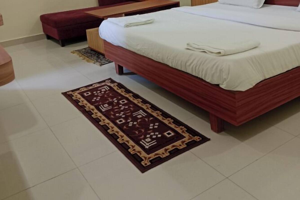 Ein Schlafzimmer mit einem Bett, einem Holz-Kopfteil, einem roten Sofa, einem kleinen Tisch und einem gemusterten Teppich.