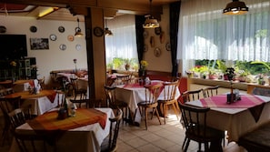 Un restaurante con varias mesas, sillas, luces colgantes y plantas en macetas.