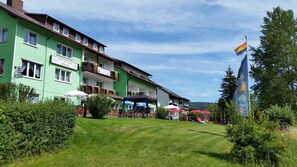 Un hotel con fachada verde, mesas al aire libre y una bandera arcoíris.
