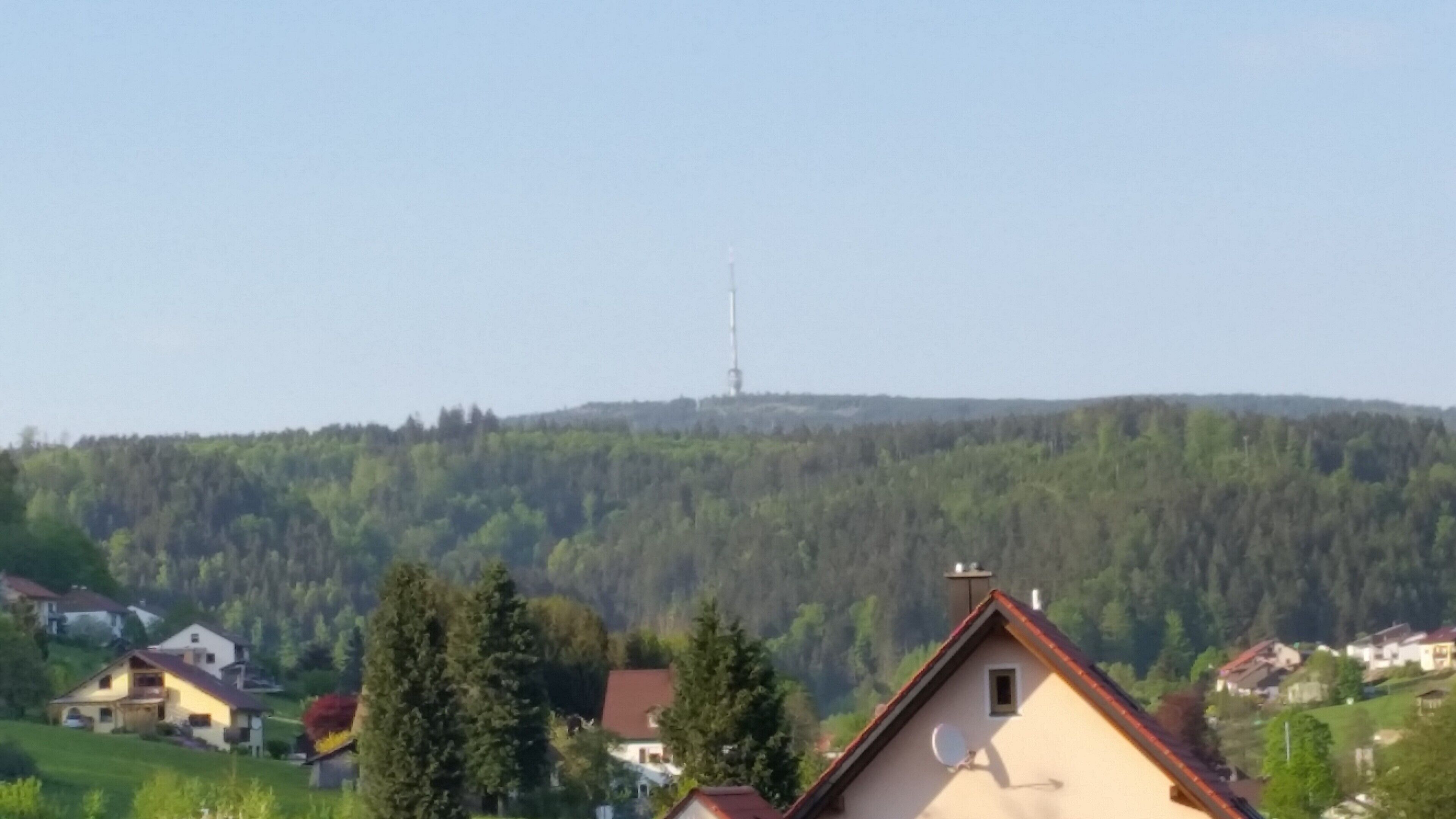 Un paysage rural avec des maisons, une colline et une tour qui se dessine à l’horizon.