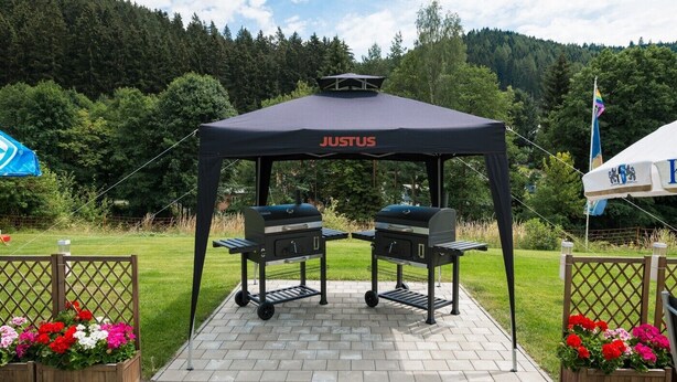 Un barbecue installé sous une tente, avec le nom de marque « JUSTUS » inscrit sur le toit.