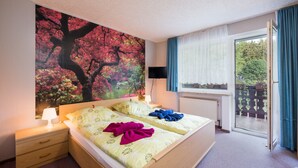 Une chambre à coucher avec un lit, une table de chevet, une télévision, une fenêtre avec des rideaux et un tableau au mur.