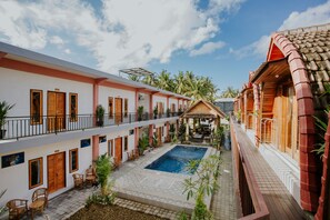 Un patio de hotel con piscina, varios balcones y zonas de estar al aire libre.