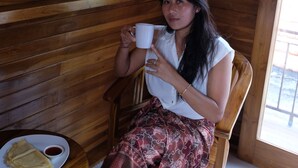 A person seated in a wooden chair, holding a white mug, with a plate of food and a cup of sauce on a small round table. - The Garuda Hostel & Accomodation (Penida Island)