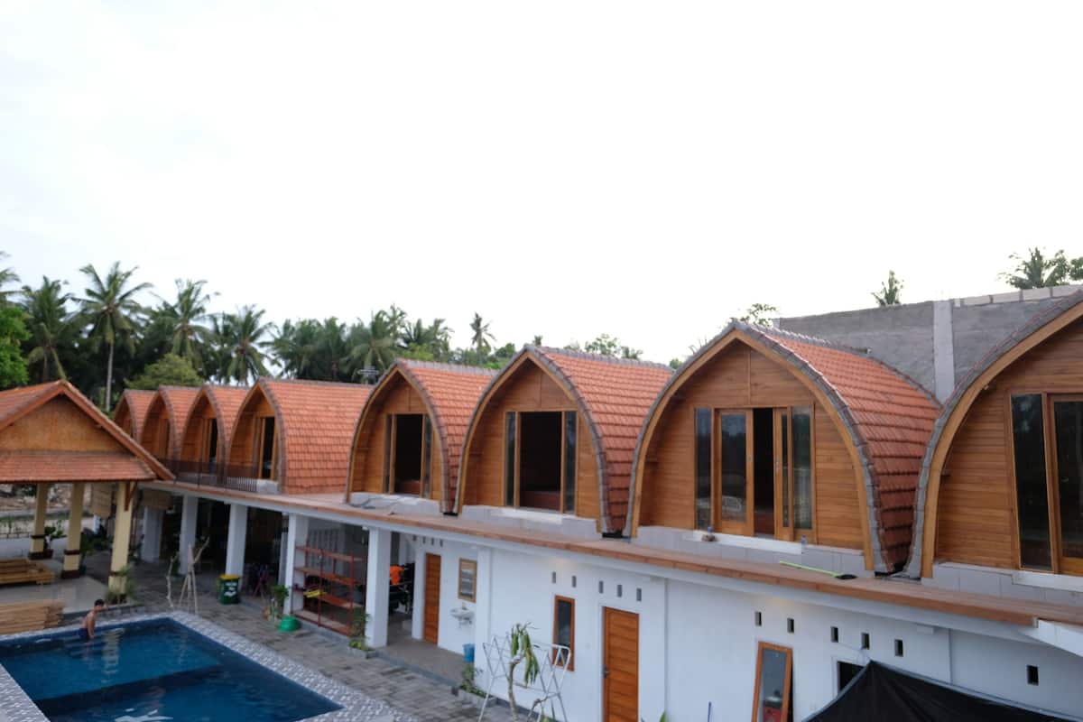 A row of wooden-roofed cabins with a pool in the foreground.