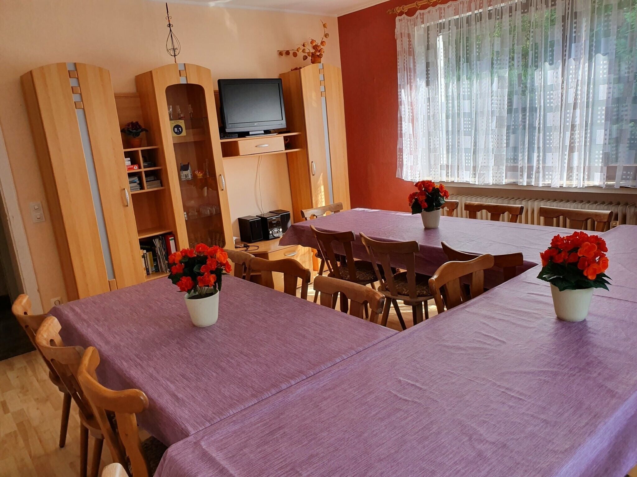 Een eetruimte met een lange tafel, stoelen en een televisie op een houten kast.