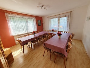 Une salle à manger avec une longue table, des chaises et deux fenêtres avec des rideaux.