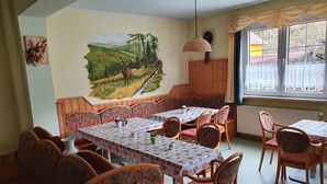A dining area with wooden tables and chairs, a mural on the wall, and a window with curtains.
