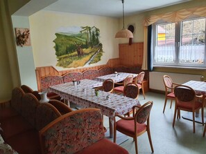 A dining area with wooden tables and chairs, a mural on the wall, and a window with curtains.
