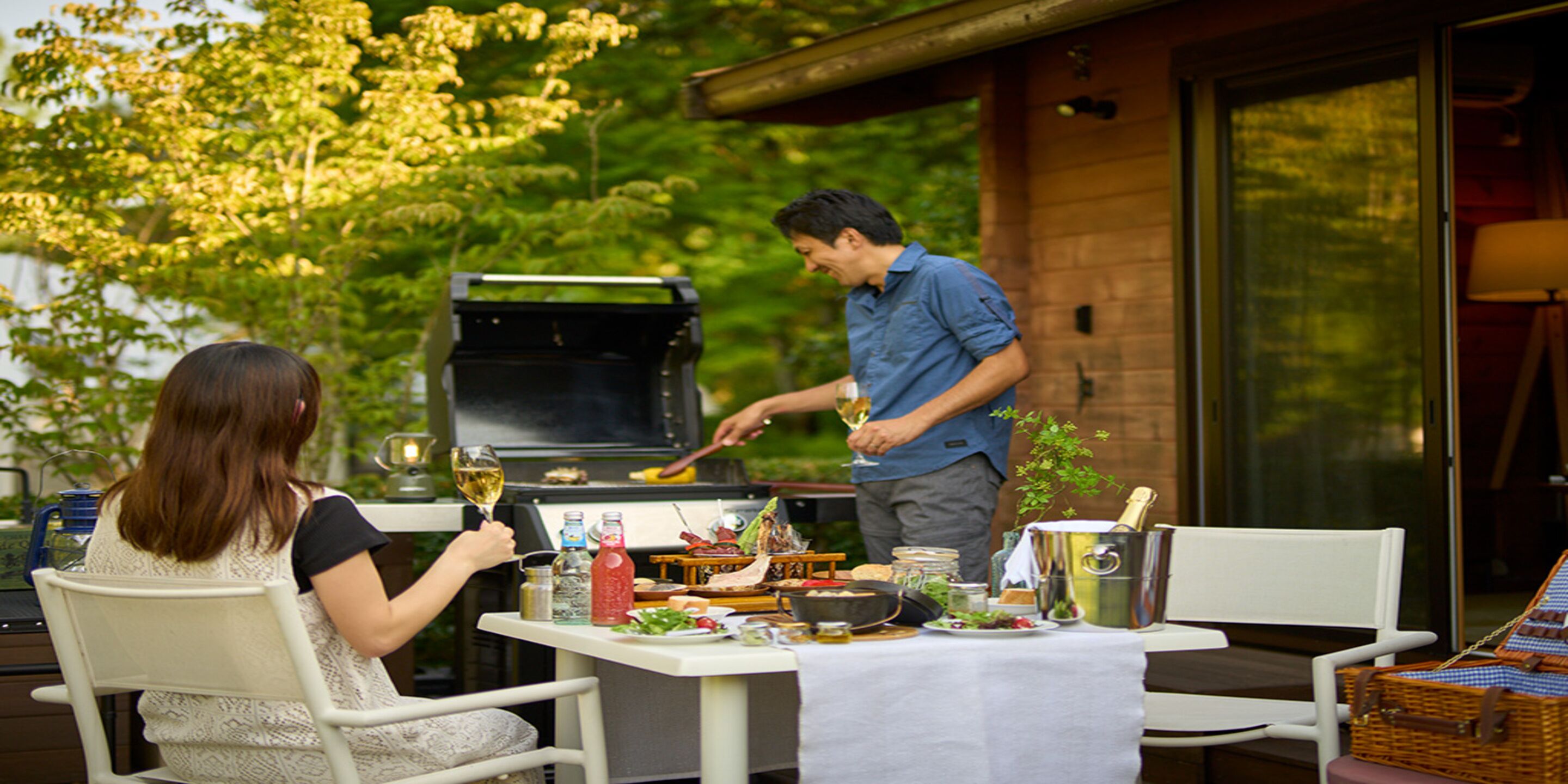 Un espacio de comedor al aire libre con una mesa dispuesta para dos personas, una parrilla y vistas a un edificio de madera.