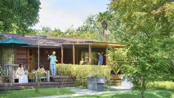 Una cabaña de madera con un porche cubierto, mobiliario exterior y un jardín bien cuidado.