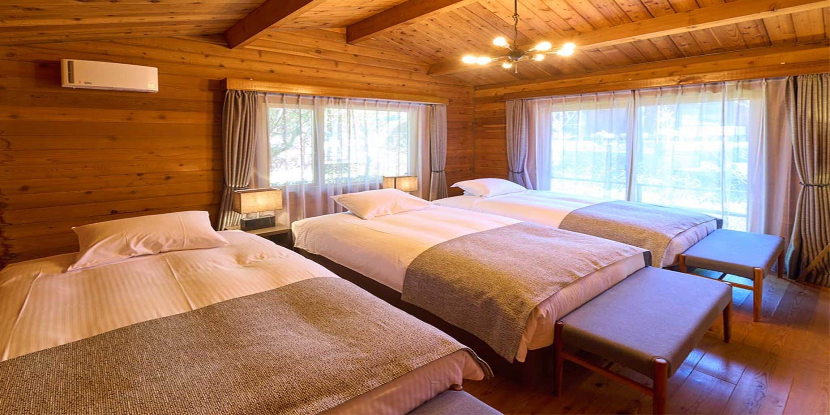 Een kamer in chaletstijl met vier bedden, houten wanden en grote ramen voorzien van gordijnen.