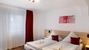 Habitación de hotel con dos camas, una cortina roja, un cuadro en la pared y suelo de madera.