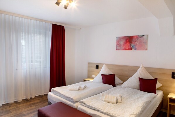 A hotel room with two beds, a red curtain, a painting on the wall, and a wooden floor.