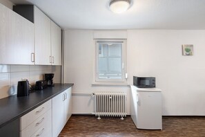 Une cuisine de taille réduite avec des meubles blancs, un four à micro-ondes encastré et une fenêtre.