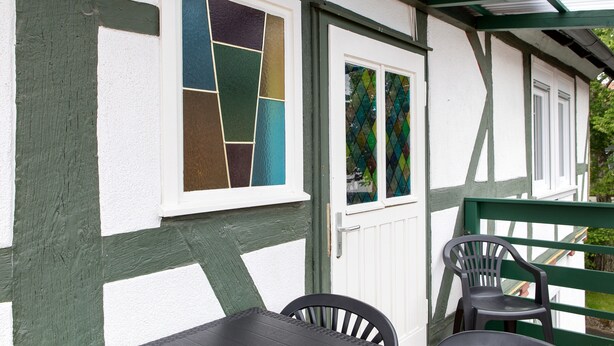 Un edificio con fachada blanca y verde, una ventana con vidrieras y una mesa con sillas.