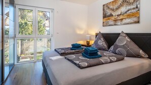 A modern bedroom with a large window, a bed with patterned pillows, and a painting on the wall.