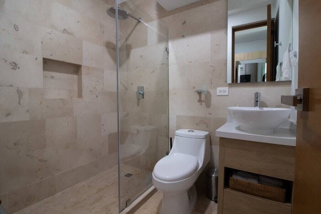 Une salle de bain moderne avec une douche à parois de verre, des toilettes blanches et un lavabo surmonté d’un miroir.