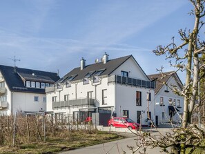 Un immeuble résidentiel avec un toit en pente, un balcon et une voiture rouge garée devant.
