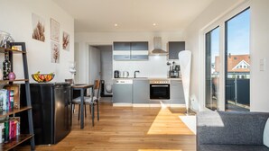 A modern kitchen with grey cabinets, a built-in oven, and a dining area with a wooden table and chairs. - Sankt Bernhard Apartment for 3 Guests (Wasserburg (Bodensee))