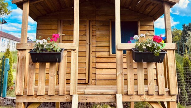 Una cabaña de madera con un porche, dos ventanas y plantas en macetas.