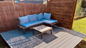 Una terraza con un sofá y una mesa, rodeada por una valla de madera y un césped.