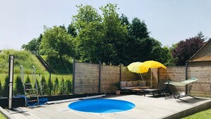 Un patio trasero con piscina, terraza de madera y zona cercada.
