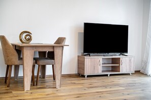 Puisesta valmistettu ruokapöytä tuoleineen, televisio, joka on sijoitettu kaapin päälle, ja spiraalimainen koriste.