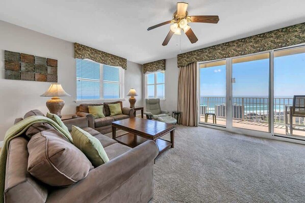 A spacious living room with a large window offering a view of the ocean, a ceiling fan, and a cozy seating area with a coffee table.