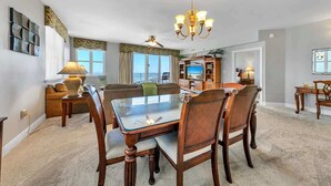 Un salón amplio con una mesa de comedor de vidrio, sillas de madera, una araña, televisión y un balcón con vistas.