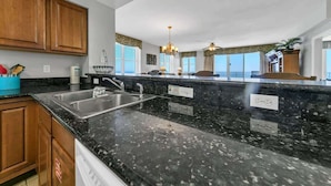 Una cocina con encimeras de granito, fregaderos de acero inoxidable, armarios de madera y una isla grande con campana extractora integrada.