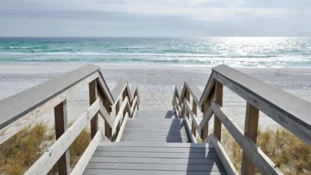 Un paseo marítimo de madera que conduce a una playa con vista clara al océano.