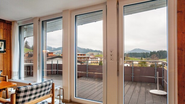 A room with a wooden bench, a table, and a view of a balcony with a railing. - Holiday Apartment "Rommel" with Mountain View, Private Terrace & Wi-Fi (Stiefenhofen)