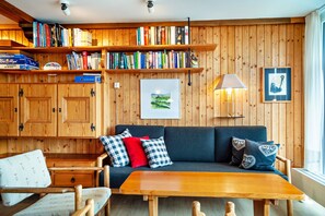 A cozy room with a wooden wall, a sofa, a table, and shelves with books.