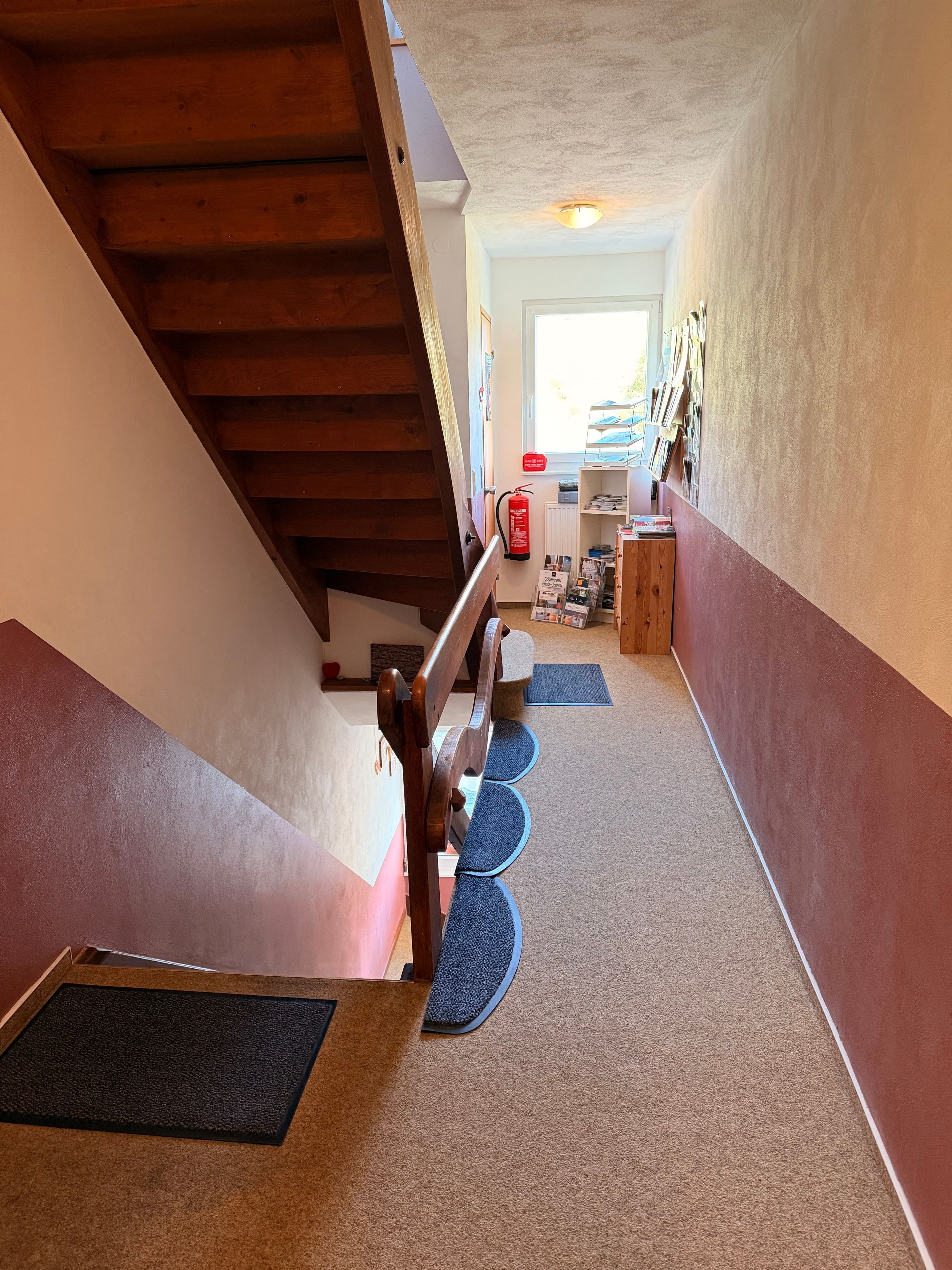 A staircase with a wooden handrail, carpeted steps, and a fire extinguisher mounted on the wall.