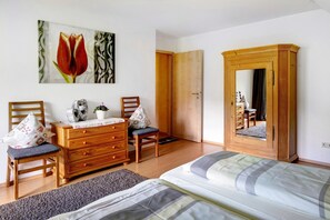 Une chambre à coucher avec un lit, une commode en bois, deux chaises, un miroir et un tableau accroché au mur.