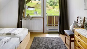 Una camera da letto con un letto, una sedia, una cassettiera, una finestra con tende e vista su un paesaggio verde.