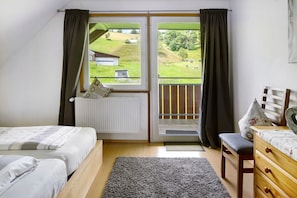 A bedroom with a bed, a chair, a dresser, a window with curtains, and a view of a green landscape.